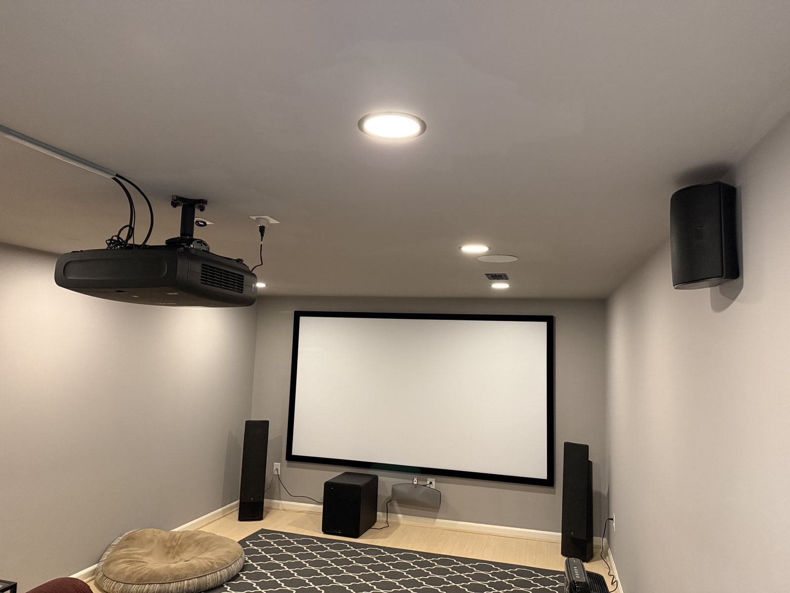Dedicated home theater with ceiling-mounted projector, drop-down screen, tower speakers, subwoofer, and in-ceiling surround speakers